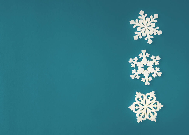 クリスマス休暇の組成物は、テキストのコピースペースとサイアンアカマリンの背景に白い雪の結晶の装飾を表示します。平置きだ。冬、ポストカードテンプレート. - 写真・画像