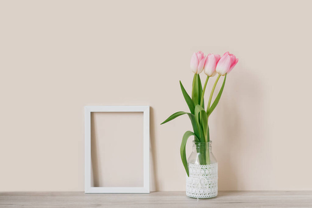 Modelo en un marco blanco con un tulipán rosa En un frasco de vidrio con encaje. Espacio para texto - Foto, Imagen