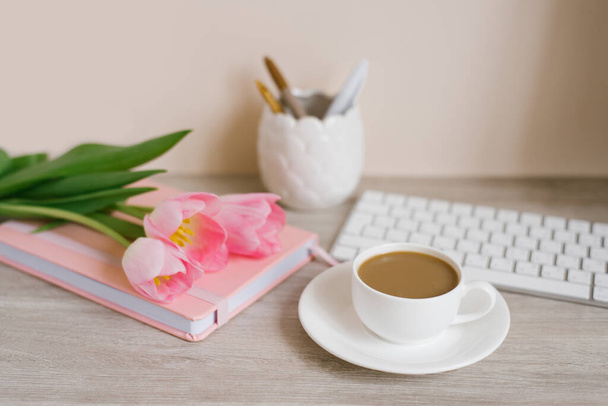 Hogar oficina lugar de trabajo: taza de café, cuaderno, teclado, flores de tulipán, cepillos, sobre fondo de madera - Foto, Imagen