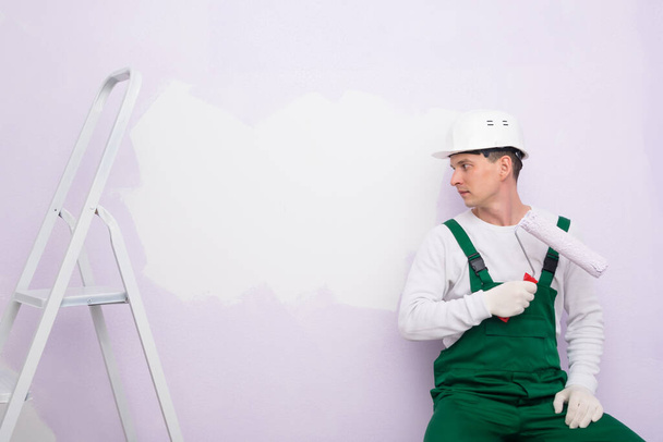 a worker with a paint roller looks at a white piece of wall - Foto, Imagem