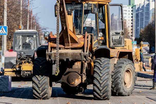 A heavy front loader transports earth in a bucket and grades the road. Road repair in the center of a modern city in autumn. Heavy construction machinery for moving soil - Photo, Image