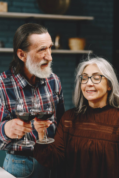 Modern senior drinking wine together in kitchen - Foto, imagen