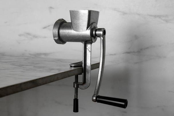 Metal manual meat grinder on table against white marble background - Foto, immagini