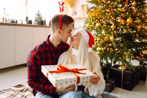 Young couple with Christmas gifts at home near Christmas tree. Romantic day. Winter holidays. New Years. - Fotografie, Obrázek