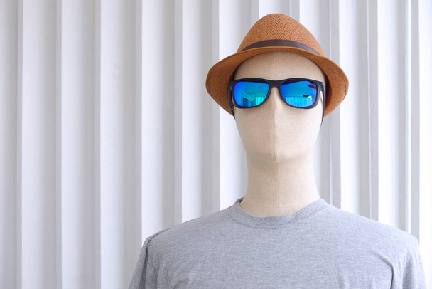Πρόσοψη ανδρικής μανεκέν σε γκρι t-shirt με γυαλιά ηλίου και καπέλο fedora σε λευκό ξύλινο φόντο  - Φωτογραφία, εικόνα