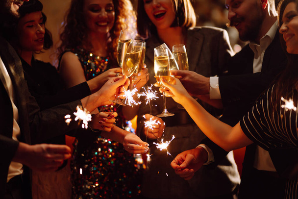 Sparkling sparklers in the hands of young friends. People  celebrate winter holidays with sparkles and champagne. Holidays, vacation, relax, party and lifestyle concept. - Valokuva, kuva