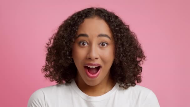 Järkyttynyt musta nainen vaihtaa lauseketta iloinen yli vaaleanpunainen tausta - Materiaali, video