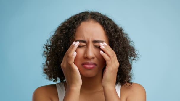 Mujer africana que masajea los ojos doloridos que sufren de dolor, fondo azul - Metraje, vídeo