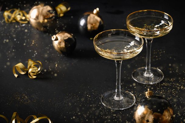 Festive New Year champagne flutes and Christmas gold baubles on black background. - Foto, afbeelding