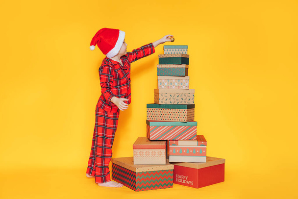 Çocuk, sarı arka plandaki bir yığın Noel hediyesine takılıyor. - Fotoğraf, Görsel
