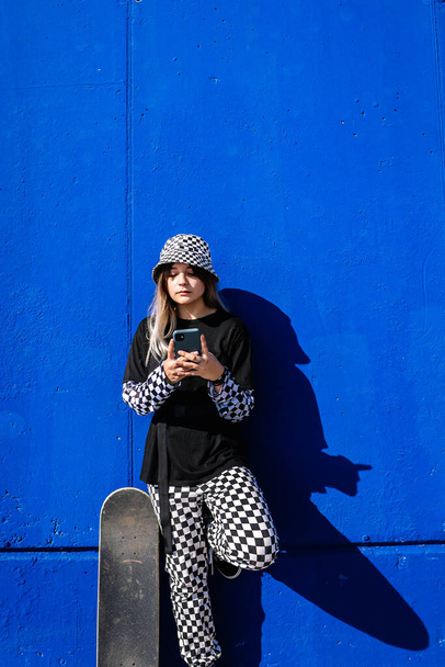 Stylish woman with skateboard browsing smartphone - Zdjęcie, obraz