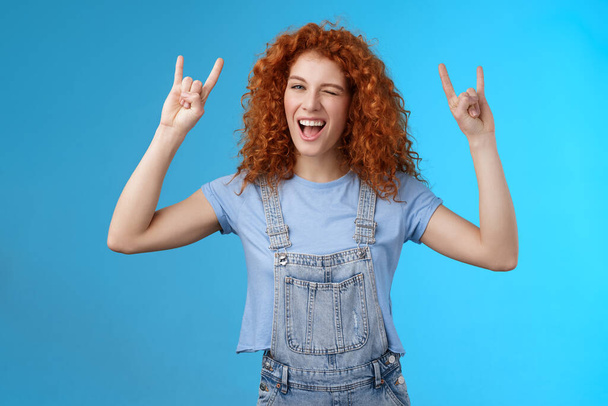 Daring cool sassy redhead ginger girl curly natural hairstyle winking joyfully yelling yeah enjoy awesome party dancing music festival show rock-n-roll heavy metal gesture have fun blue background - Photo, Image