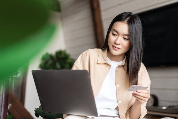 Retrato de chica asiática comprando en el sitio web con ordenador portátil y tarjeta de crédito. Mujer joven compra en línea, sentado en casa y de compras en Internet - Foto, imagen