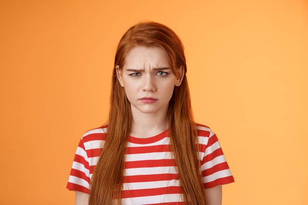 Close-up moody upset childish redhead girl, sulking unfair situation, frowning upset, complaining disappointed, pouting offended, stand uneasy perplexed orange background, whining displeased - Fotó, kép