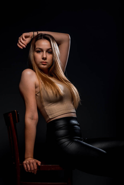 Attraente giovane modello femminile in posa in pantaloni di pelle nera mentre seduto sul loro - Foto, immagini