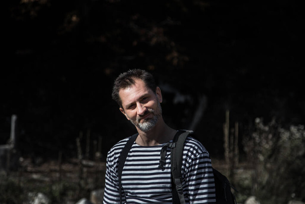 un hombre de mediana edad de unos 40 años con el pelo corto y oscuro y una barba gris, sonriendo sobre un oscuro fondo borroso - Foto, Imagen