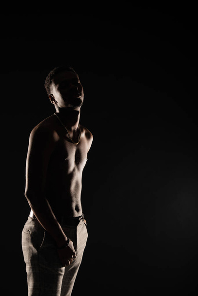 Joven negro macho es en topless mientras posando sobre fondo oscuro, silueta - Foto, Imagen