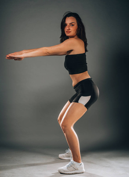 Beautiful caucasian slim woman is doing stretching training in dark modern studio - Photo, Image