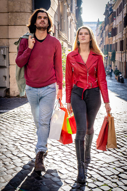 Beautiful couple traveling to Rome. Young couple went shopping and walks through the streets of the historic center with colored bags. Shopping concept. - Photo, Image