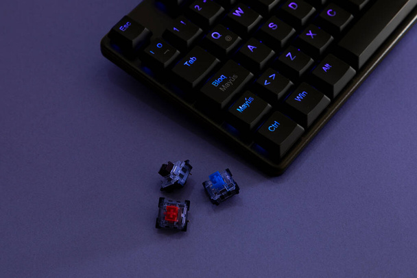 Механическая клавиатура Rgb для геймеров на столе с фиолетовым светом и выключателями сбоку - Фото, изображение
