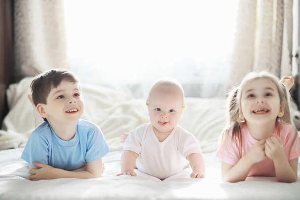 I bambini sono sdraiati sul letto accanto al neonato, sorellina. Emozioni dei bambini. - Foto, immagini