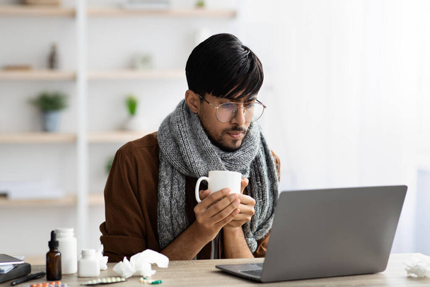 Nemocný muž ze Středního východu pracuje na laptopu, drží pohár - Fotografie, Obrázek
