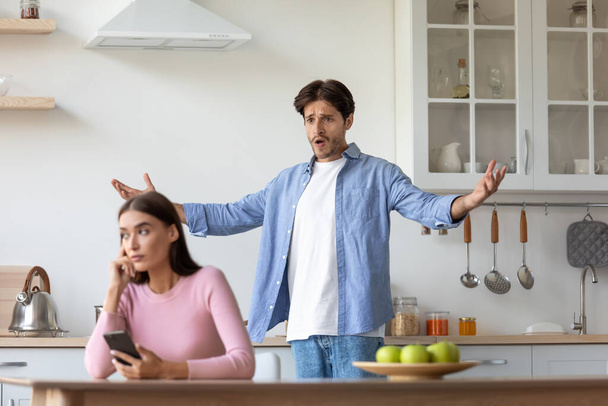 Sad young european woman with smartphone ignores offended angry screaming gesticulating husband - Фото, изображение