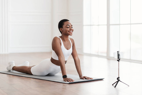 Young african woman stretching back on mat with cellphone - Photo, Image