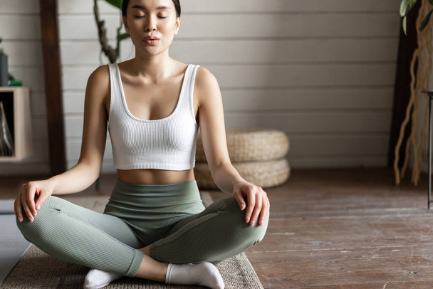 Primer plano de chica asiática joven, atleta de fitness en casa haciendo ejercicio en alfombra de piso, meditación y estiramiento, ejercicios de yoga - Foto, Imagen