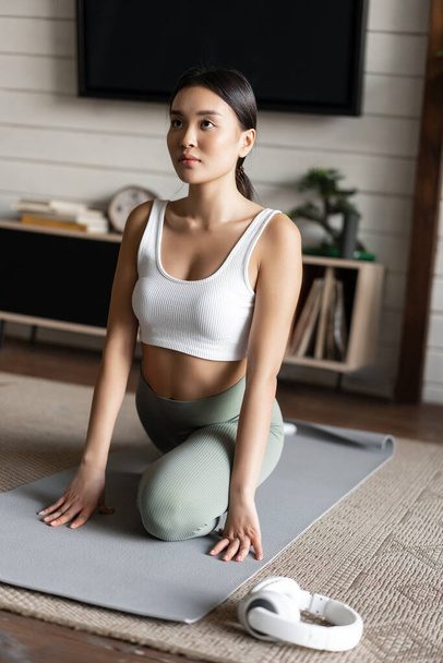 Asiatisches Mädchen macht Yoga Stretching zu Hause, Workout in ihrem Wohnzimmer, trägt Aktivkleidung - Foto, Bild
