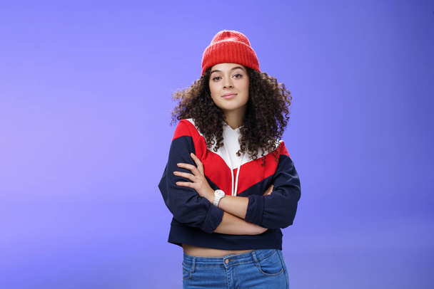 Girl will show winter who boss. Confident and stylish self-assured attractive woman with curly hair in cute red beanie and warm sweatshirt holding hands crossed over chest and looking daring at camera - Photo, Image