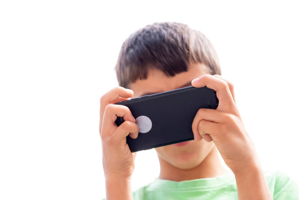 ένα παιδί που παίζει με ένα έξυπνο τηλέφωνο με το πρόσωπό της καλυμμένο από το κινητό τηλέφωνο, χέρια σε πρώτο πλάνο με επιλεκτική εστίαση, οριζόντια - Φωτογραφία, εικόνα