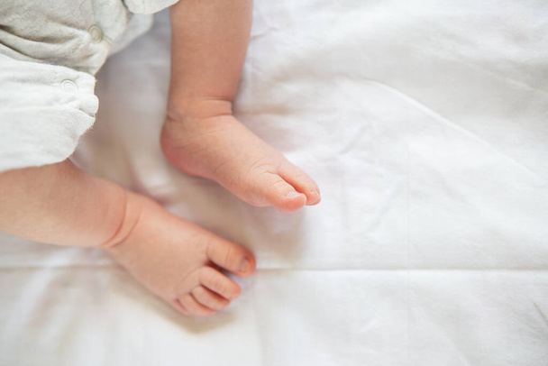 Маленькие ноги новорожденного ребенка на кровати, вид сверху. Концепция материнства, грудного вскармливания - Фото, изображение