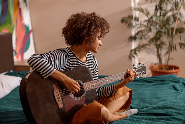 Multiracial young woman playing guitar at home - Foto, imagen