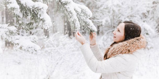 Zimowy portret młodej kobiety. Szczęśliwa dziewczyna spacery w lesie zimowym i patrząc śnieg spada. Święta Bożego Narodzenia i Nowy Rok. Wolne życie. Cute lady w ciepłej odzieży o zabawy w przyrodzie na świeżym powietrzu. - Zdjęcie, obraz