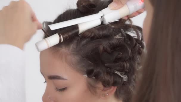 Un coiffeur fait une coiffure pour une jeune belle fille aux cheveux longs et foncés - Séquence, vidéo