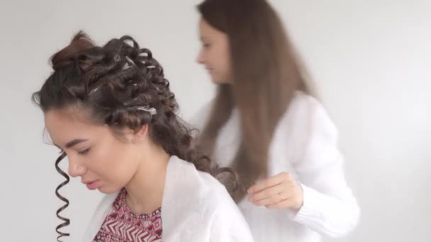 Kadeřník dělá účes pro mladou krásnou dívku s dlouhými tmavými vlasy - Záběry, video