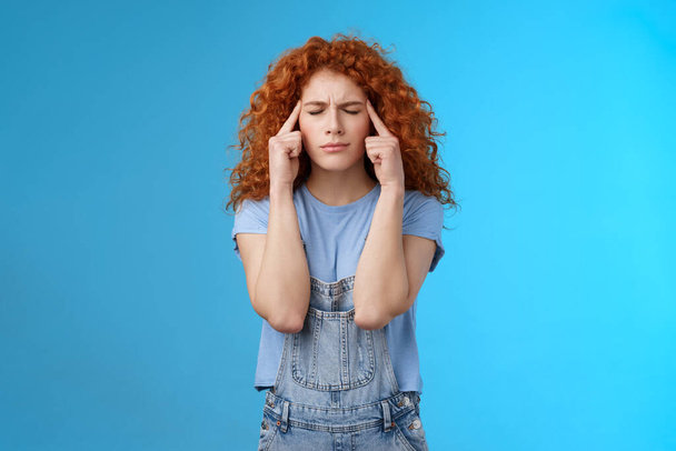 Come on girl think. Perplexed distressed concerned intense redhead curly woman close eyes frowning touch temples suffer migraine painful headache cannot concentrate blue background - Photo, Image