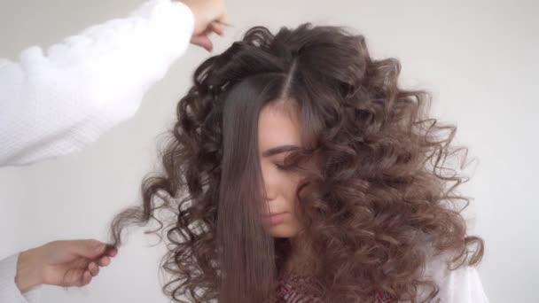 Hiusstylisti tekee kampauksen nuorelle kauniille tytölle, jolla on pitkät tummat hiukset - Materiaali, video