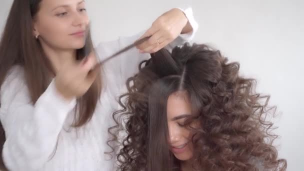 Kadeřník dělá účes pro mladou krásnou dívku s dlouhými tmavými vlasy - Záběry, video
