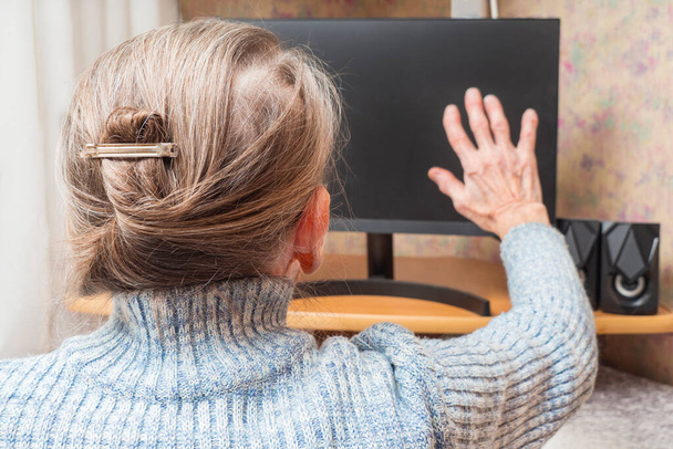 Una donna anziana saluta o saluta con la mano sullo schermo del computer. Il concetto di comunicazione video su Internet. Comunicazione a distanza con la famiglia in quarantena. - Foto, immagini