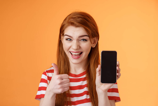Cheerful assertive redhead woman recommend smartphone app, show phone display, thumb-up like approval sign, smiling broadly, suggest good online purchase, mobile advertisement - Foto, immagini