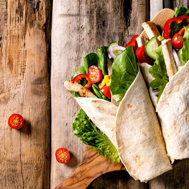 Traditional mexican tortila wrap with pork meat and vegetables on wooden cutting board over brown wooden background. Top view, flat lay. Copy space. Homemade fast food. Square image - Φωτογραφία, εικόνα