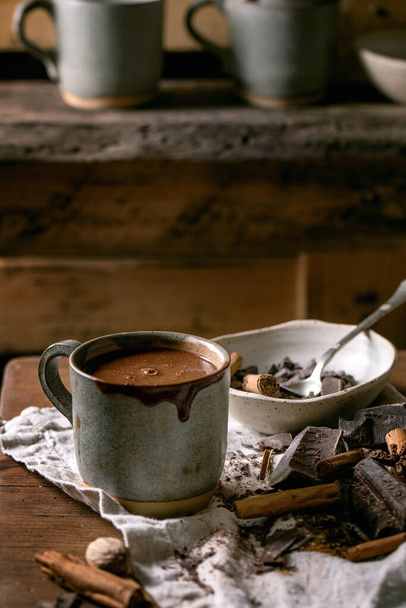 Cup of hot spicy homemade chocolate winter drink with chopped dark chocolate and ingredients on rustic linen tablecloth. Country kitchen table. Warm cozy drink. - Фото, изображение