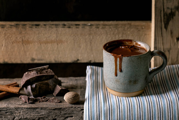 Cup of hot spicy homemade chocolate winter drink on linen napkin with chopped dark chocolate bar and spices on old wooden shelf. Warm cozy drink. - Foto, Imagen