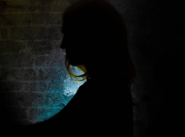古い石の暗い壁の近くにブロンドの髪の女性のシルエット - 写真・画像