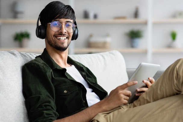 Joyeux Moyen-Orient jeune homme refroidissant à la maison avec tablette - Photo, image