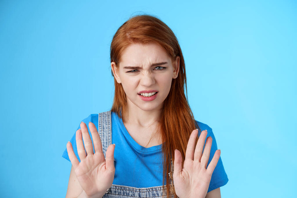 Close-up uninterested displeased ignorant picky redhead girlfriend, frowning make disgusted grimace raise hands block stop gesture, refuse, waving arms no rejection sign, stand blue background - Foto, afbeelding