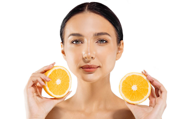 Woman and fruit portrait. A happy model holds a juicy orange near her face and looks at the camera on a white background. Beautiful girl uses citrus fruits and natural vitamins for healthy skin - Photo, Image