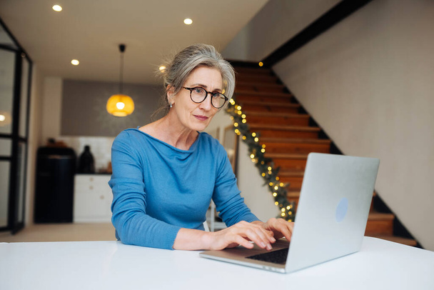 Mutlu orta yaşlı kadın dizüstü bilgisayara bakıyor. - Fotoğraf, Görsel